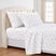 A neatly made bed with a white bedding set featuring a delicate pink and green floral print, styled with two matching pillowcases in front of a tufted cream headboard. #color_rose-whisper-white