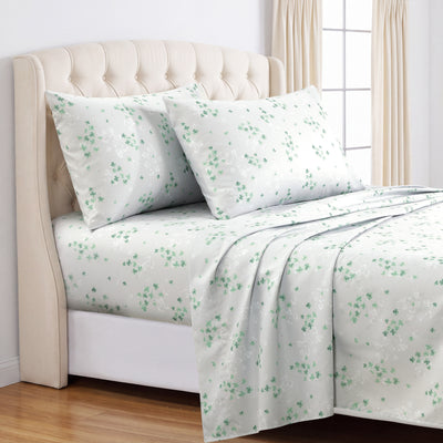 A neatly made bed with a white sheet set and matching pillowcases featuring a delicate green floral pattern, styled in a bright bedroom with a cream tufted headboard and window curtains. #color_shamrock-breeze-light-gray