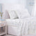 White bedding set with a delicate blue and green floral print, styled on a bed with a white upholstered headboard, a light wood nightstand, and a soft window curtain. #color_soft-bloom-blue