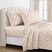 A neatly made bed with a cream sheet set featuring a delicate tan leaf pattern, styled with matching pillowcases and a tufted cream headboard in a bright bedroom. #color_willow-grove-rust