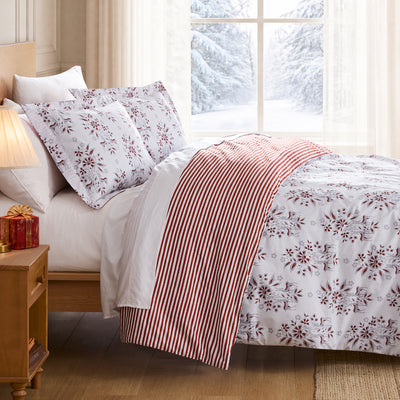 Merry Manor duvet cover set styled on a Christmas bed with white floral print, red striped reverse, matching shams, and festive decor.