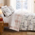 Frosted Pines duvet cover set styled on a bed with ivory winter forest print, pink plaid reverse, matching shams, and Christmas decor.