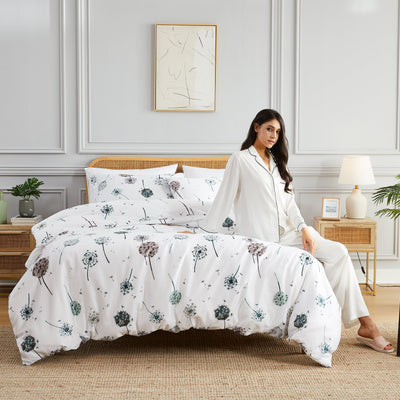 Lady sitting on bed with Dandelion Dreams Duvet Cover in White#color_dandelion-white