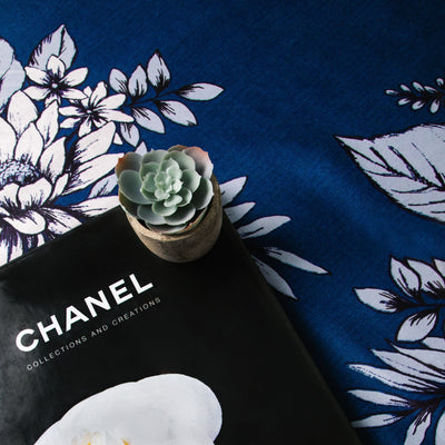 Details of Flora Extra Deep Pocket Sheet Set in Blue with a magazine and plant over it.#color_flora-blue