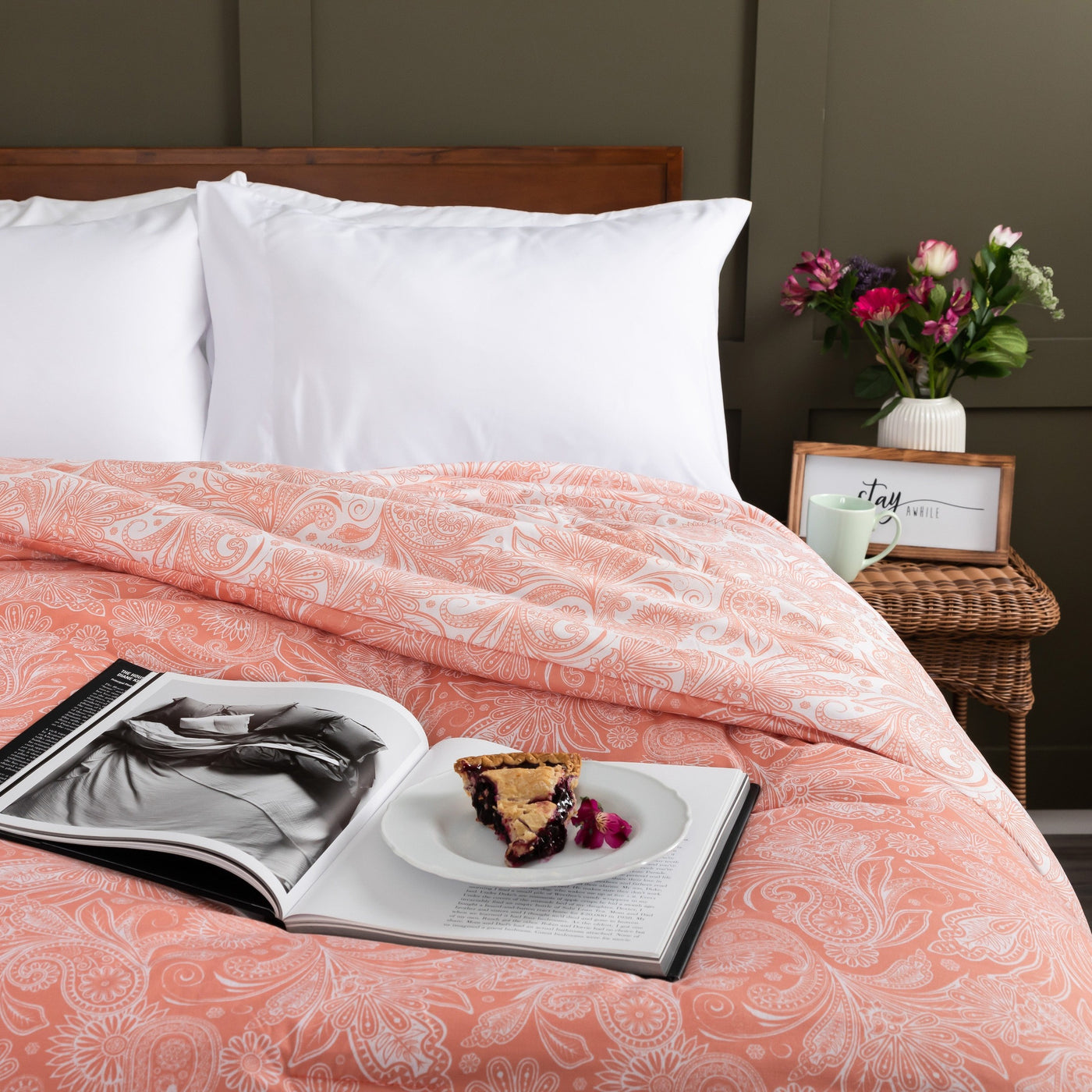 Half Front View of Perfect Paisley Reversible Comforter Set in Coral with Magazine and plate of pie on top#color_perfect-paisley-coral-haze