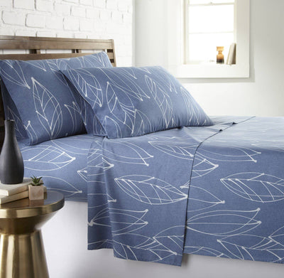 Angled view of Modern Foliage sheet set showcasing blue sheets with white leaf print on a made bed with wooden headboard
